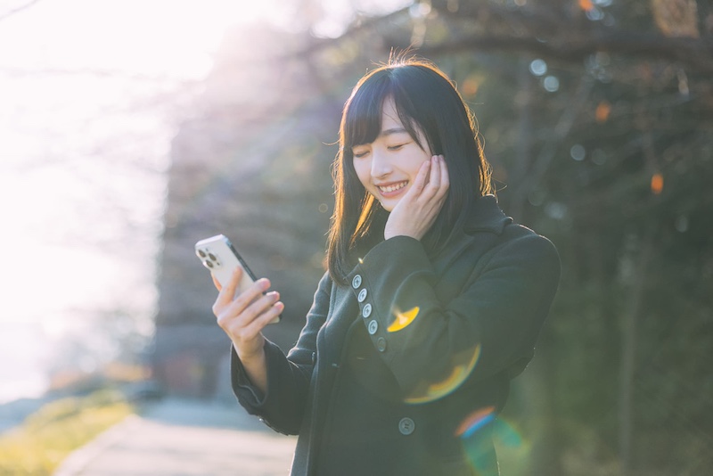 スマホを見て微笑む女性の画像